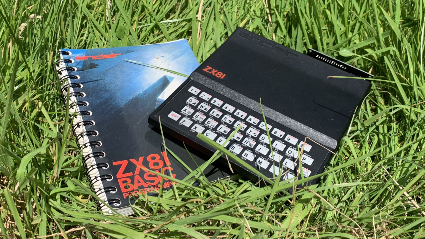 ZX81 with a caseless RAM Pack and a spiral-bound book "ZX81 BASIC Programming", sat on grass