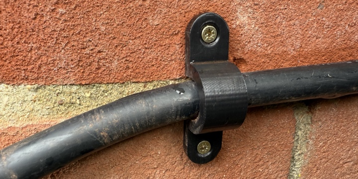 A thick cable attached to a brick wall by a 3D-printed clip